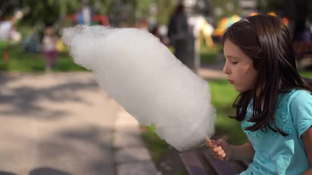 可爱的小女孩坐在公园的长椅上吃棉花糖视频素材