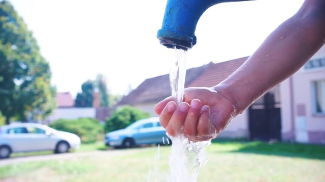 男孩用手从水龙头里洒水。在一个炎热的夏天度假玩视频素材