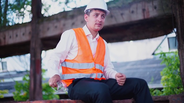 一个穿着背心的工程师准备在建筑工地工作，戴上头盔。视频下载