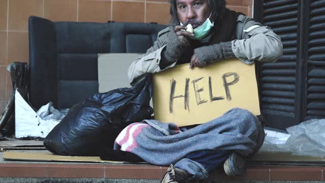 无家可归的乞丐手拿着钱在大街上乞求帮助。视频素材