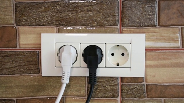 一名男子用手将多个家用设备连接和断开，连接到一个三倍电源插座上。视频下载