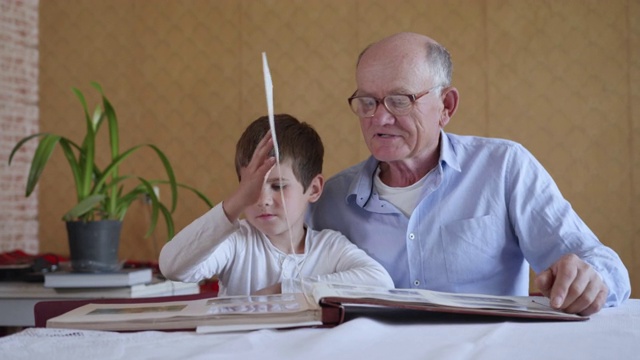 一位戴着眼镜的老人和他的孙子一起享受着家庭相册的美好回忆坐在房间的桌子前视频下载