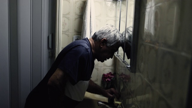 绝望的60岁老人把头靠在浴室的镜子上，绝望而悲伤视频素材