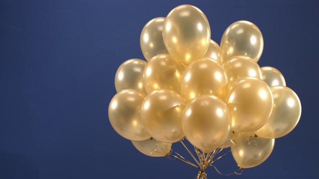 装饰元素——金色气球——在视频中旋转，作为节日的惊喜:在蓝色背景下，情人节、生日、圣诞节或新年。视频素材