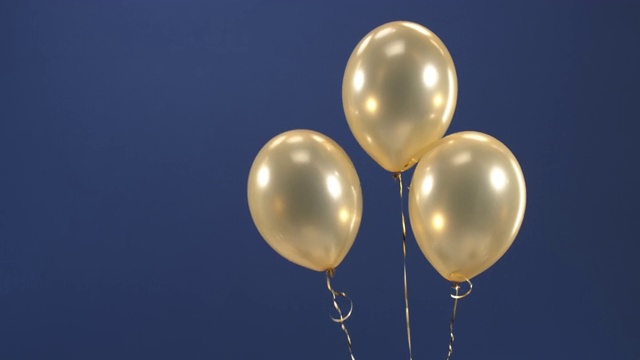 一个装饰元素——三个金色气球——出现在视频中，作为节日礼物:在蓝色背景下的情人节、生日、圣诞节或新年。视频素材