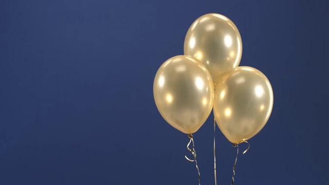 装饰元素——三个金色气球——悬浮在滚轴上，作为情人节、生日、圣诞节或新年的蓝色背景礼物。视频素材