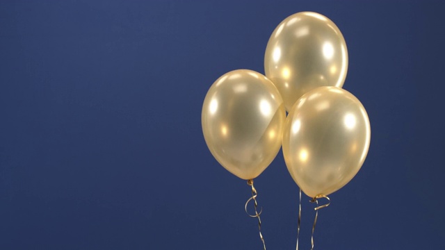 这个装饰元素——三个金色气球——出现在视频中，作为情人节、生日、圣诞节或新年的蓝色背景礼物。视频素材