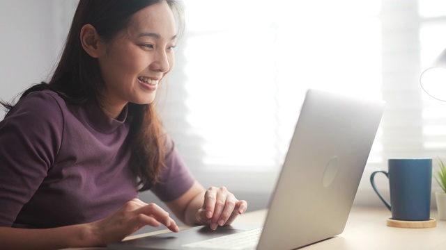 微笑的亚洲年轻女子在笔记本电脑上打字视频下载