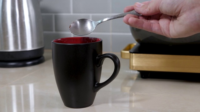 浓缩的速溶咖啡颗粒倒入厨房桌子上的黑色陶瓷杯中视频下载