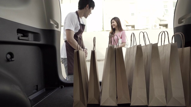 4K超高清多莉拍摄:两名搬运工或搬运工将购物袋带到汽车上，在接送站为顾客。视频下载