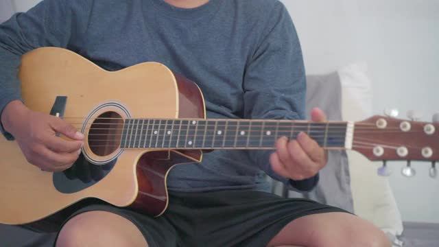 特写男人们正在自己的床上练习弹奏吉他。视频下载
