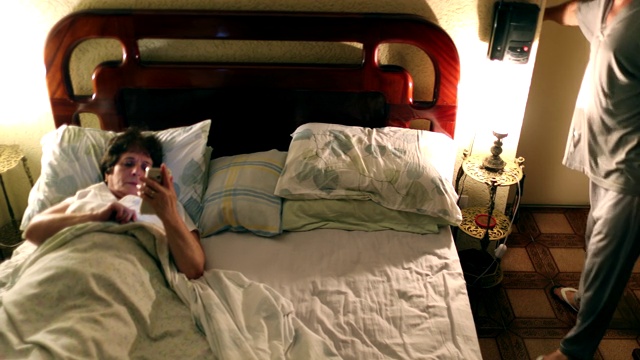 已婚夫妇在晚上仪式上床睡觉。年长的妻子在用手机，丈夫躺下关掉灯视频下载