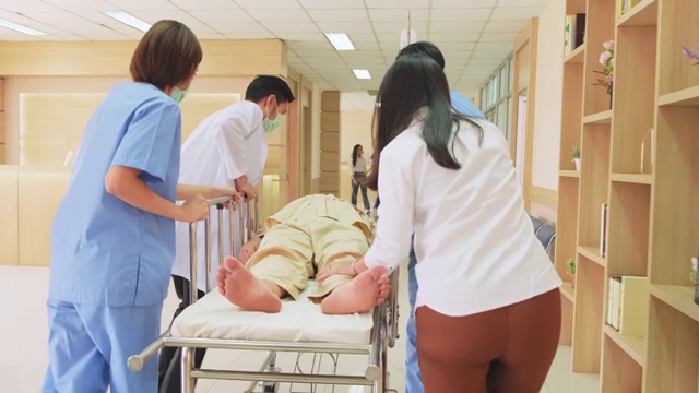 一组医生、护士和外科医生在医院走廊抬着躺在担架上的重伤病人。医护人员急忙将急诊老病人转移到手术室。视频下载