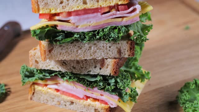 夹着火腿、奶酪、蔬菜和羽衣甘蓝在木板上吃三明治。视频下载