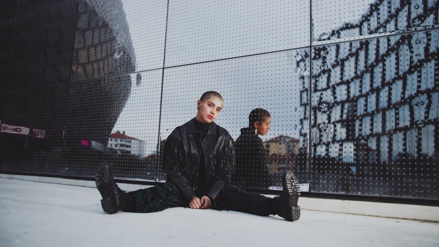 手持拍摄的时尚女性潮人坐在人行道上对着玻璃建筑视频素材