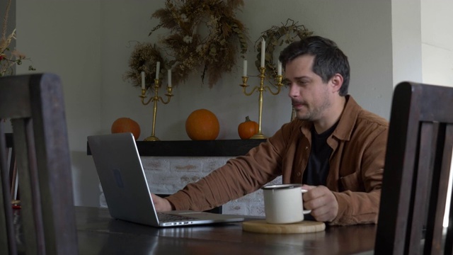 男人在家里用笔记本电脑工作，喝着茶视频下载
