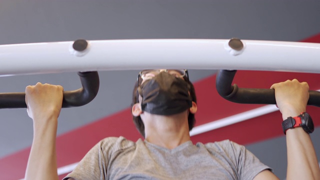 在冠状病毒感染的情况下，亚洲男子戴上口罩在健身房做引体向上视频下载