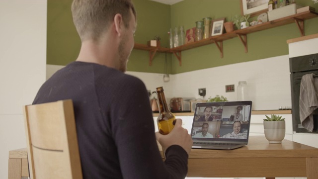 男性使用视频通话技术在厨房桌子上与朋友在笔记本电脑上享受饮料视频素材