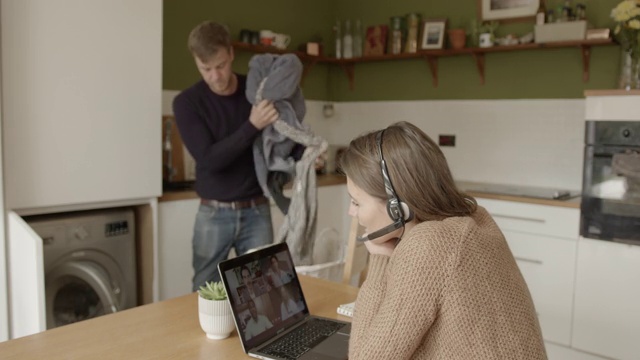 女性在家用笔记本电脑进行视频通话，男性在厨房洗衣服视频下载