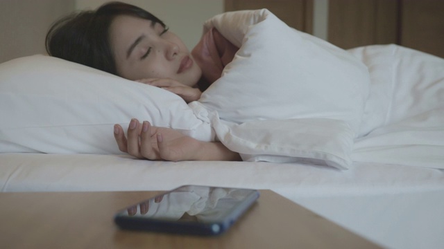Scene of asian woman waking up because of alarming on the phone. Then she turn the alarm off and go back to sleep视频素材