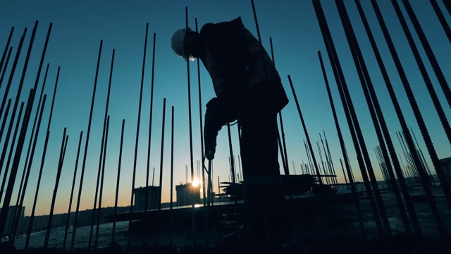 建筑者在日落的背景上用钻头工作。视频素材
