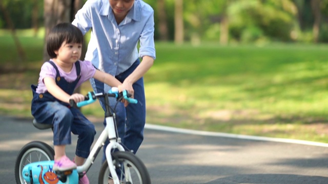 亚洲小女孩学习骑自行车与年轻的母亲在花园视频下载