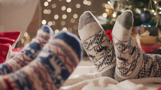 两个人坐在地板上的毯子上，在圣诞袜里移动他们的脚视频下载