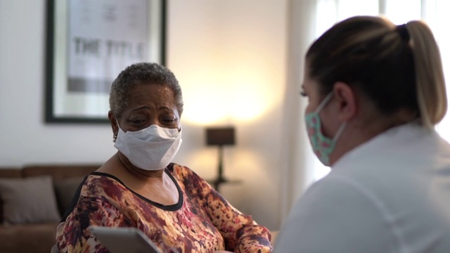医生在老年妇女病人家中与她交谈-使用口罩视频下载