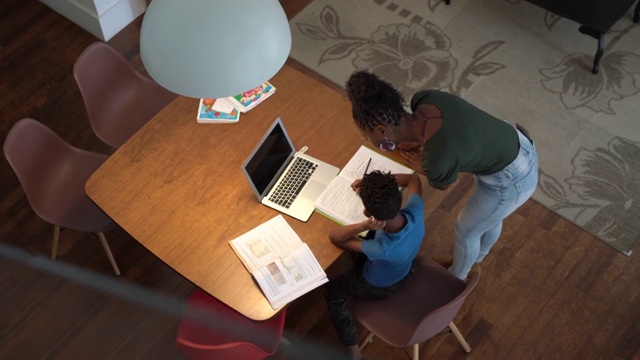 高角度的母亲帮助儿子使用笔记本电脑在家上学视频素材