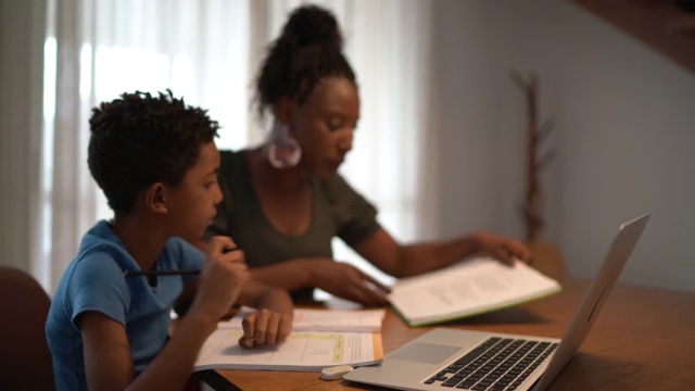 母亲帮助儿子使用笔记本电脑在家学习视频素材