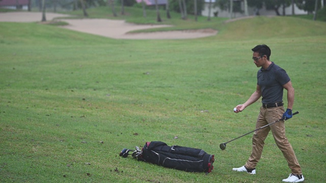 下雨天，亚洲华人男性高尔夫球手在高尔夫球场开球点从高尔夫球袋中挑选高尔夫球杆开球视频下载