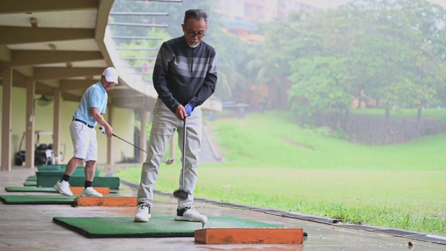 亚洲华人活跃的高级男子高尔夫球手在高尔夫练习场开球和挥杆他的潜水高尔夫球杆视频素材