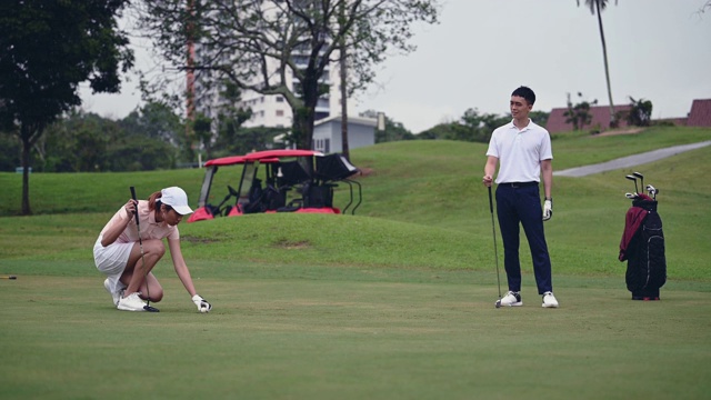 亚洲中国女高尔夫球手与男伙伴在高尔夫球场上看球视频素材