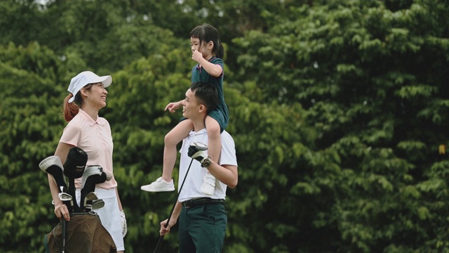 亚洲中国年轻的家庭高尔夫球手在绿色球场亲密时间，而父亲背着他的女儿在肩膀上视频下载