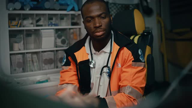 严肃的黑人非裔美国医护人员戴上蓝色外科橡胶手套在一辆受伤病人的救护车上。紧急医疗技术员正在检查受害者的生命体征视频下载
