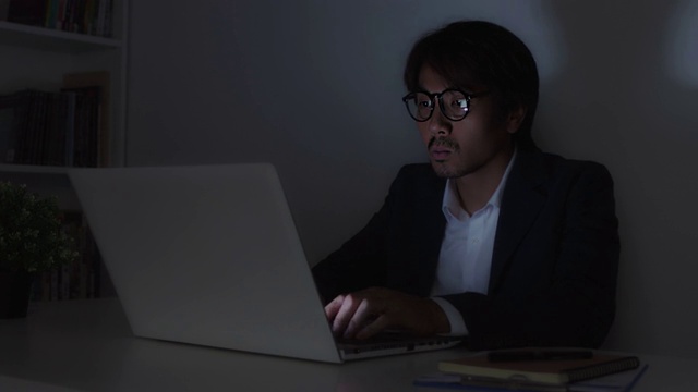 亚洲保险代理人商人戴眼镜摸下巴和打字笔记本电脑在办公室工作到很晚视频下载