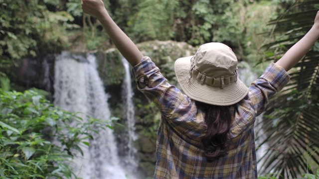 年轻女子与背包享受热带瀑布景观视频素材