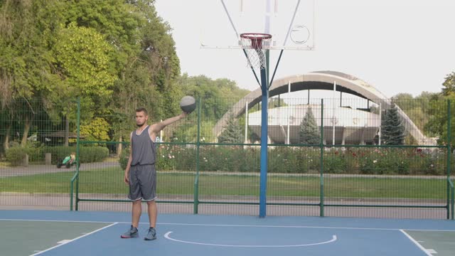 这个年轻人在公园的球场上成功地投篮球。运动员练习街球。关闭了。慢动作视频下载
