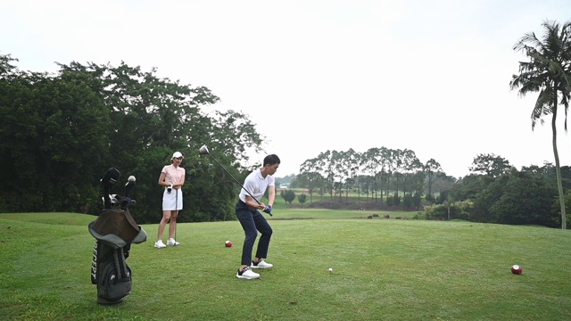 慢镜头:亚洲华裔男子高尔夫球手在球场上开球，他的妻子在旁边视频素材
