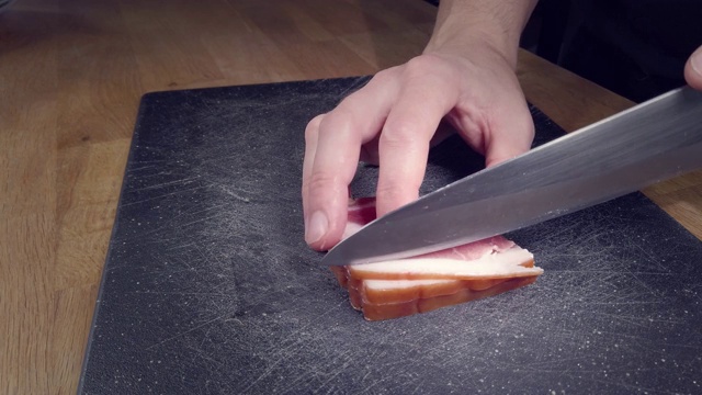 一个左撇子用一把大菜刀把肥肉切成薄片，放在厨房的木板上视频下载