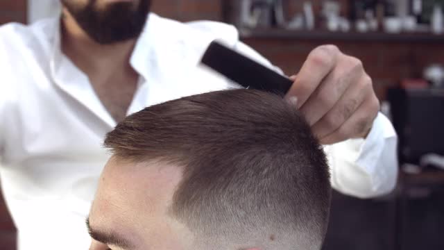 近景细心英俊的年轻理发师用胡子轻轻剪着头发视频素材