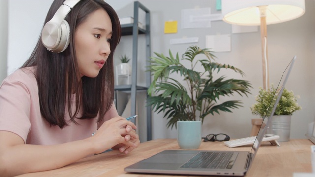 亚洲女商人戴着耳机用笔记本电脑与同事进行视频通话，并在网上讨论商业项目。视频素材