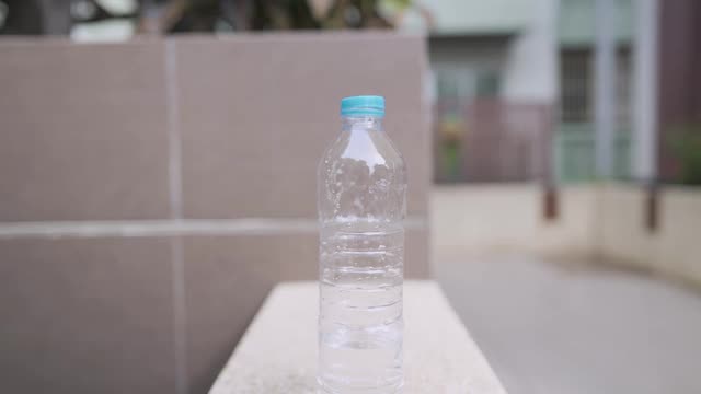 年轻美丽的亚洲女人穿白色运动服喝塑料瓶里的水，在阳光明媚的日子里绕着家附近跑，脂肪燃烧有氧运动，提神饮料，口渴的年轻健康女人休息视频下载