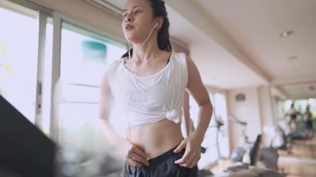 年轻美丽的亚洲女人独自在跑步机上跑步在公共健身房，做有氧运动，减肥训练计划，现代健康生活，耐力活力，流汗的女人，日光温暖的一天视频素材