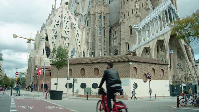 2019冠状病毒病危机期间巴塞罗那圣家堂前的自行车道。人们骑着电动车戴着口罩视频素材