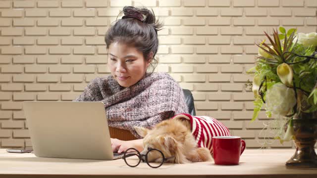 亚洲女性使用笔记本电脑在线会议在家里工作，而她的狗睡在附近的工作桌上。居家工作生活方式隔离工作隔离期新常态观念视频素材