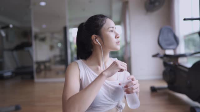 亚洲年轻漂亮的女人喝水从塑料瓶休息后在健身房锻炼，提神饮料，休息，保持水分健康健康的活力视频素材