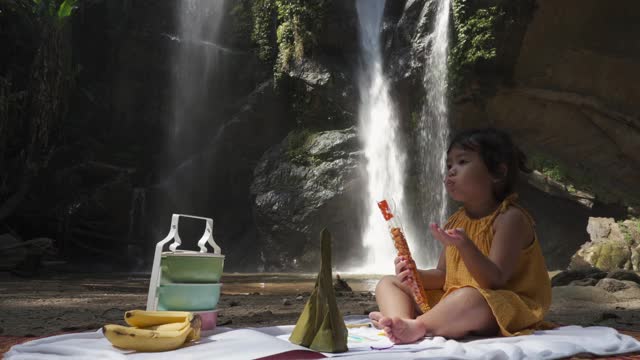 可爱的小女孩坐在瀑布边吃零食视频下载
