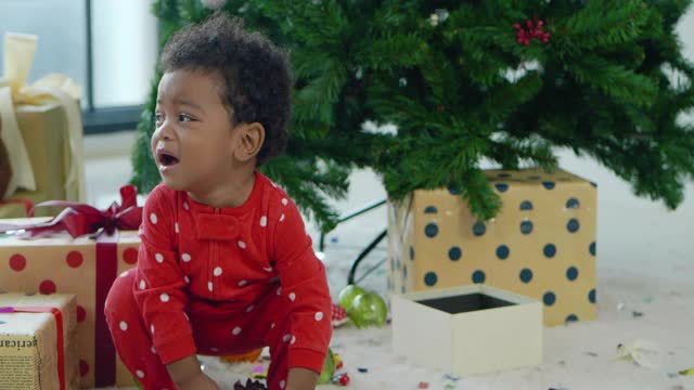 4个月大的非洲裔男婴的肖像，在圣诞树下放置礼物时打开圣诞礼盒时的失望情绪。圣诞精神的概念。视频素材