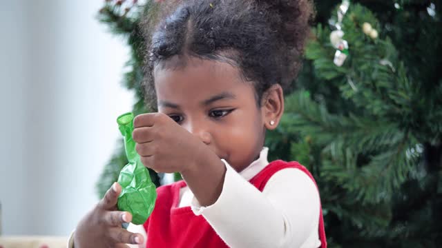 3岁的非洲裔小女孩穿着红色的衣服吹起绿色的气球，在圣诞节在家里快乐和有趣。亲密的圣诞节的概念。视频素材